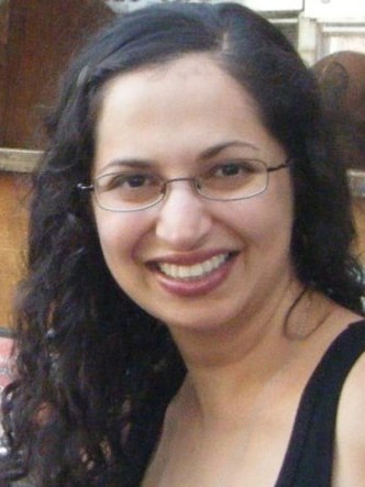A woman with glasses and long dark hair smiles at the camera