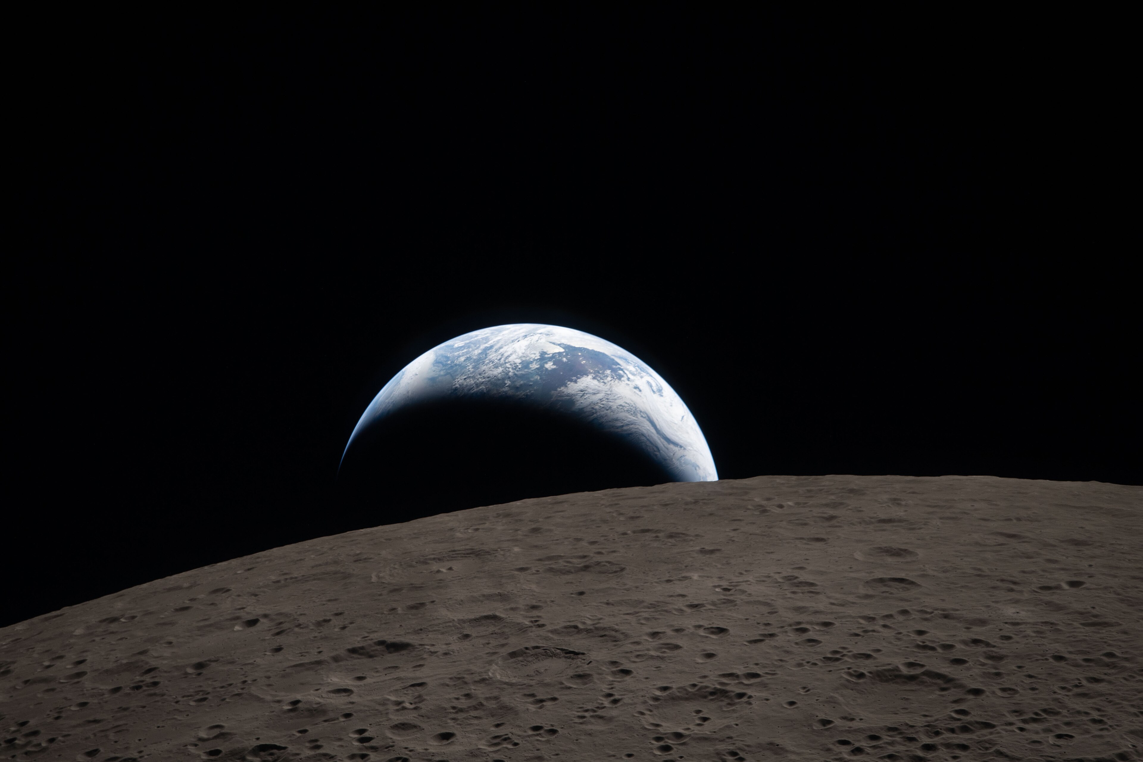 A photo taken from orbit over the moon, with Earth peeking above the moon's horizon.
