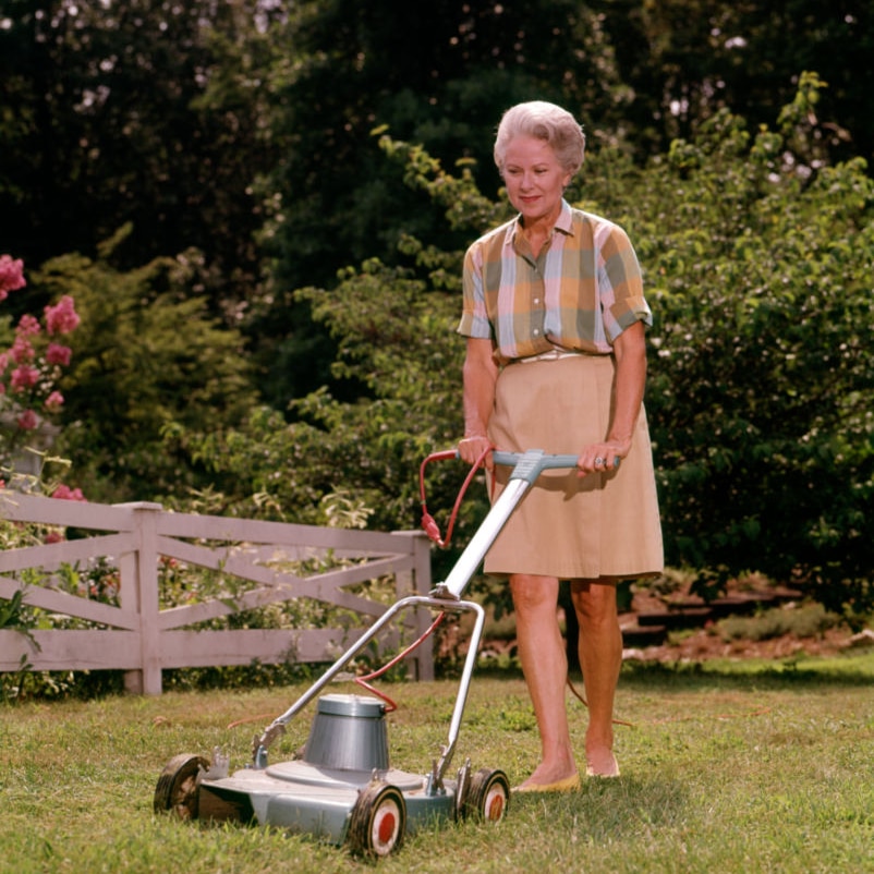 A woman mows the lawn is the 19602 in a dress.