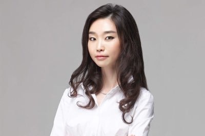 A woman with long hair wearing a white shirt with her arms crossed.