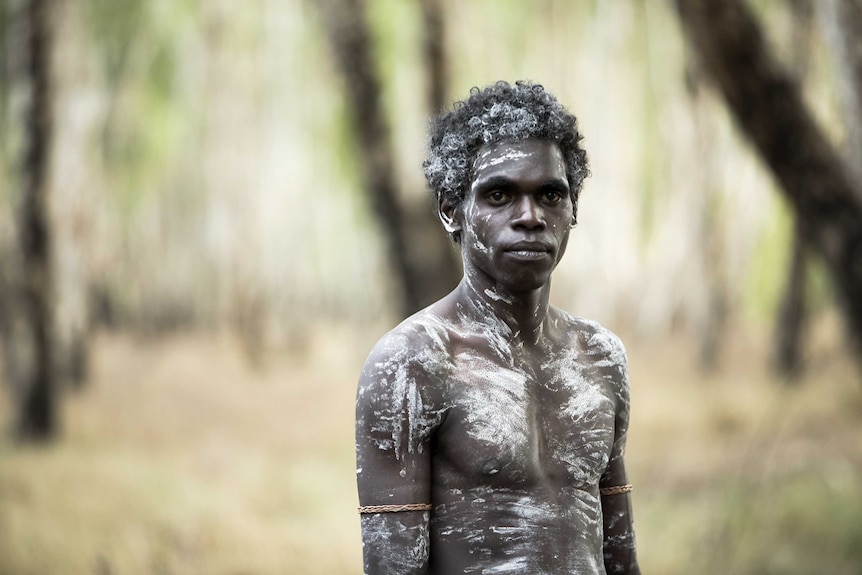 A still from the film High Ground of actor Jacob Junior Nayinggul standing in the NT outback, ceremonially painted