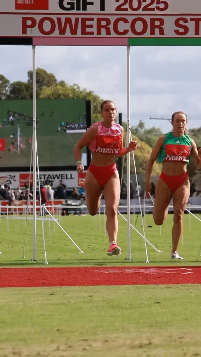 Two young women in athletics gear race down a track.