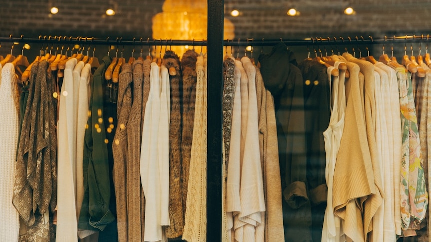 Clothes hang on hangers at a clothing retail shop.