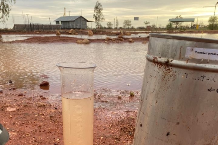 A rain gauge. In the background of the photo is water on the ground.