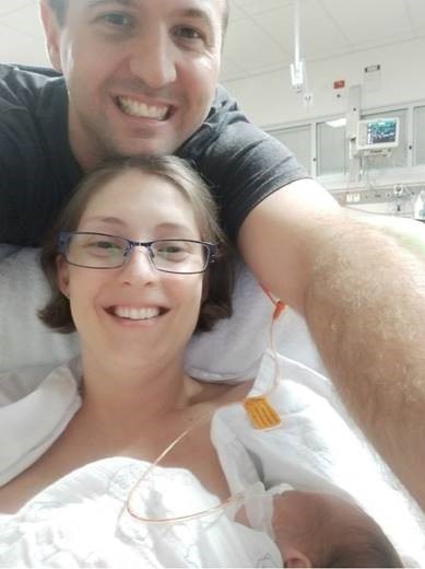 A couple in hospital gowns holding a newborn baby