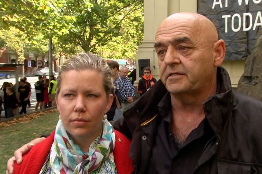 A bald man with his arm around a woman wearing a bright top.