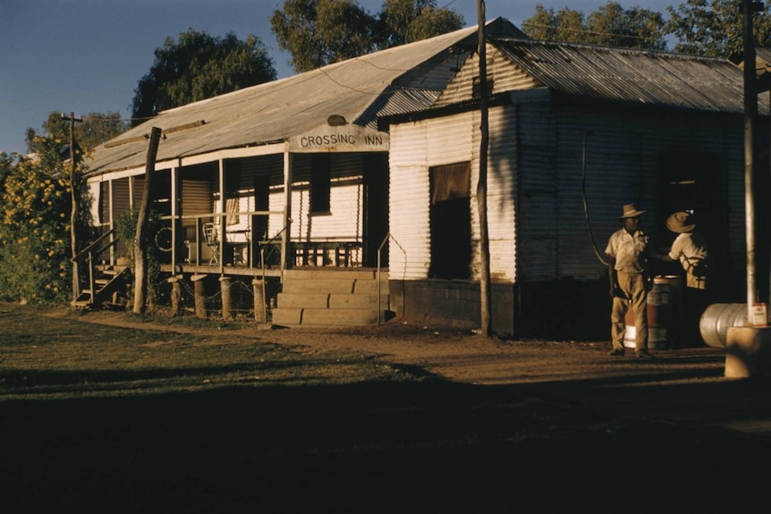 An old white building with two Indigenous men standing outside.