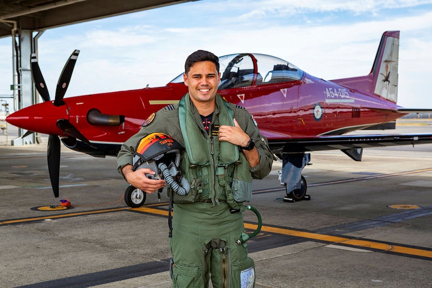 A man in a uniform stands infront of a plane 