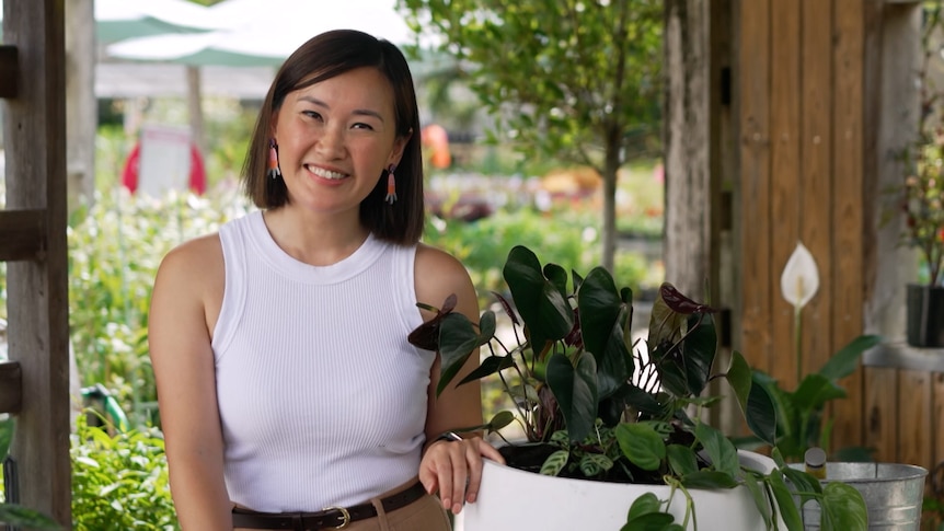 Gardening Australia's Tammy Huynh smiles next to a pot with indoor plants.