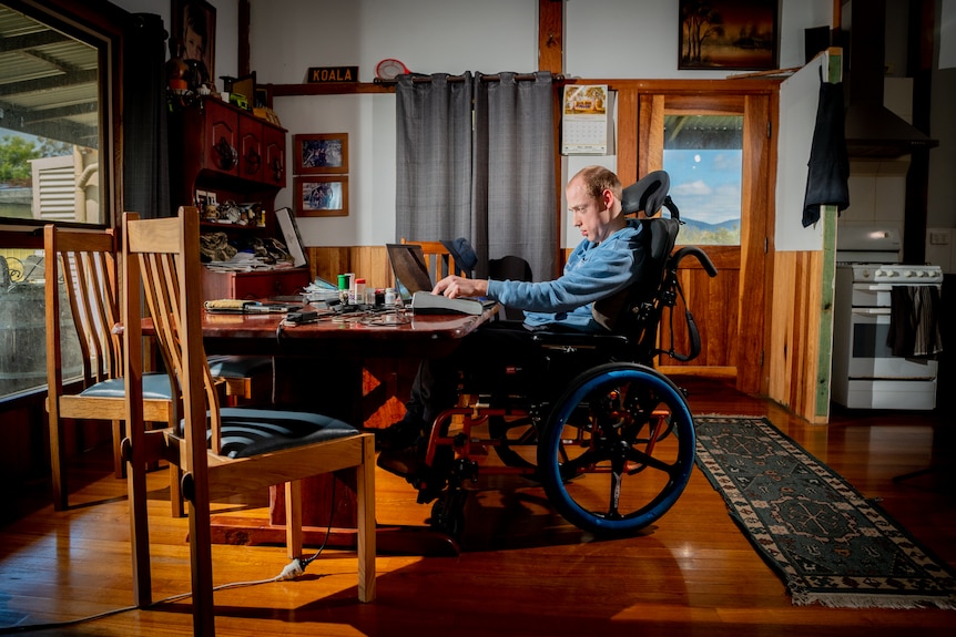 Nathan working from a wooden dining table in a rustic dining room, a hilly landscape is visible through a window.