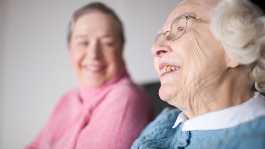 An elderly woman in glasses sits next to a younger woman
