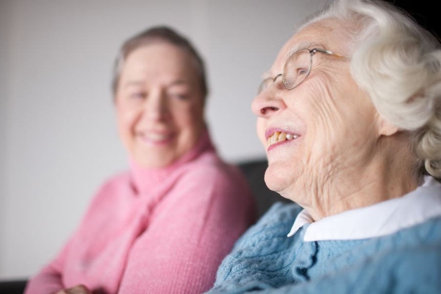 An elderly woman in glasses sits next to a younger woman