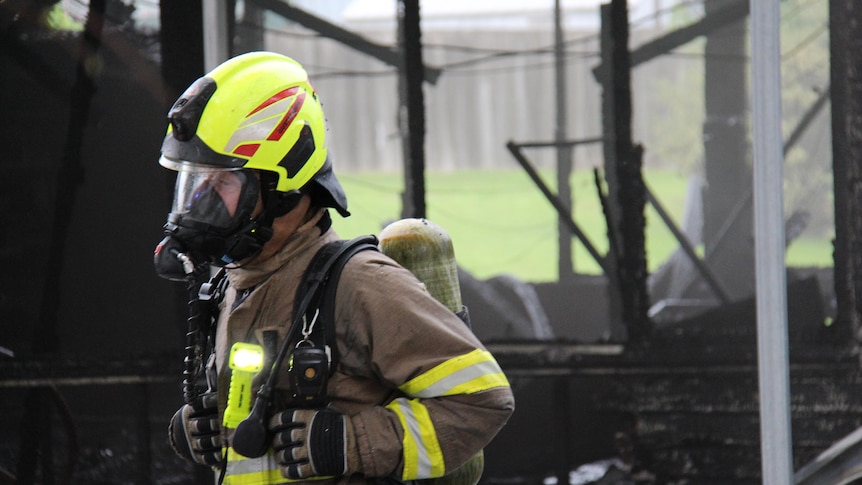A Tasmania Fire Service crew member wearing breathing apparatus in front of a blackened classroom