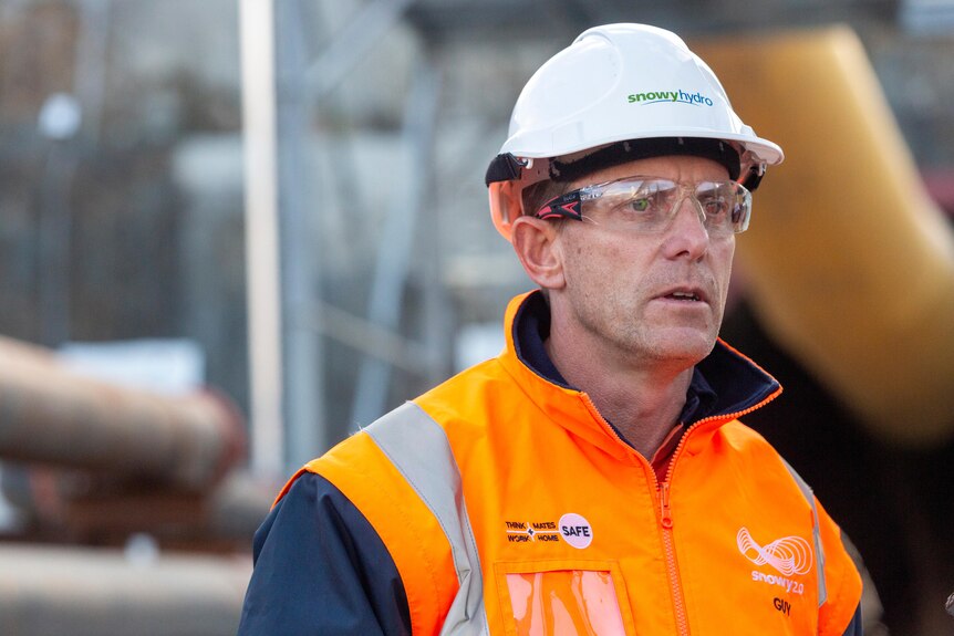 a middle-aged man wearing a hard hat outside of a tunnel