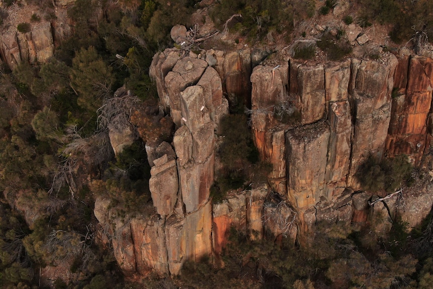 A drone shot of a rock wall with a large boulder secured by wires.