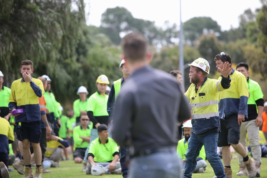 Workers in hi-vis clothing gathered on grass at Curtin University with one in a hard hat with his arms raised.