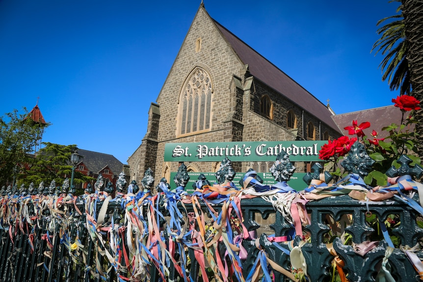 A fence in front of a Ballarat cathedral is covered in colourful ribbons. 
