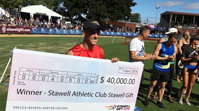 A young man holds an oversized winner's cheque at the Stawell Gift running race in Western Victoria.