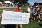 A young man holds an oversized winner's cheque at the Stawell Gift running race in Western Victoria.
