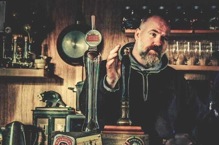 Tasmanian man Dave Kok behind the bar at The Outpost bar on East Burra island, Shetland, Scotland.