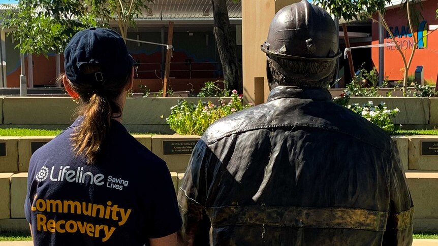 Woman in Lifeline shirt sits next to brass miner statue