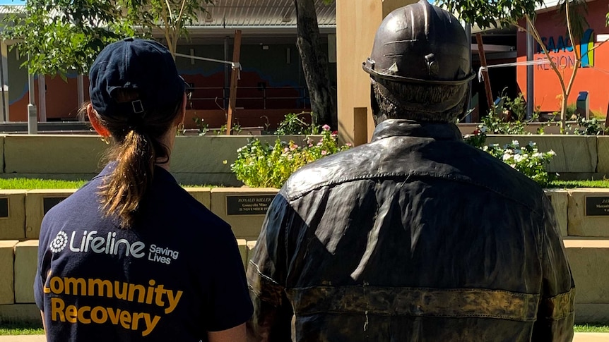 Woman in Lifeline shirt sits next to brass miner statue.