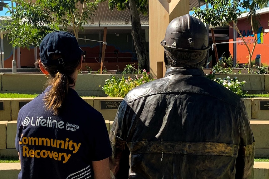 Woman in Lifeline shirt sits next to brass miner statue