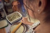 A photograph of a woman rolling out paratha, with her face obscured.