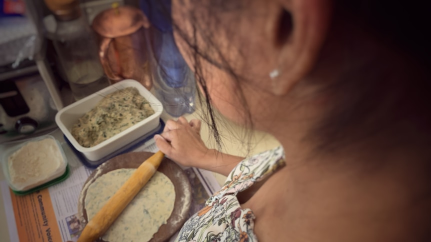 A photograph of a woman rolling out paratha, with her face obscured.