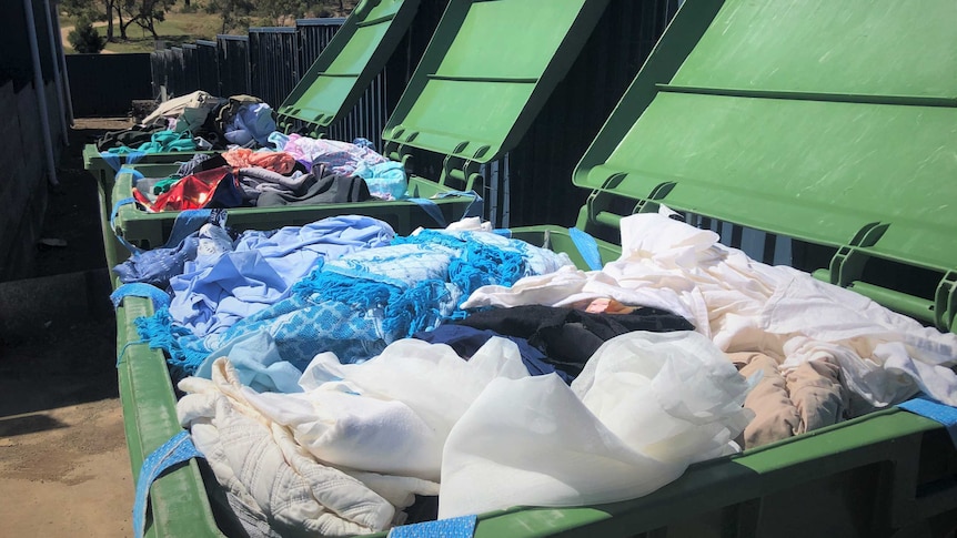 Three large green bins full of clothing.