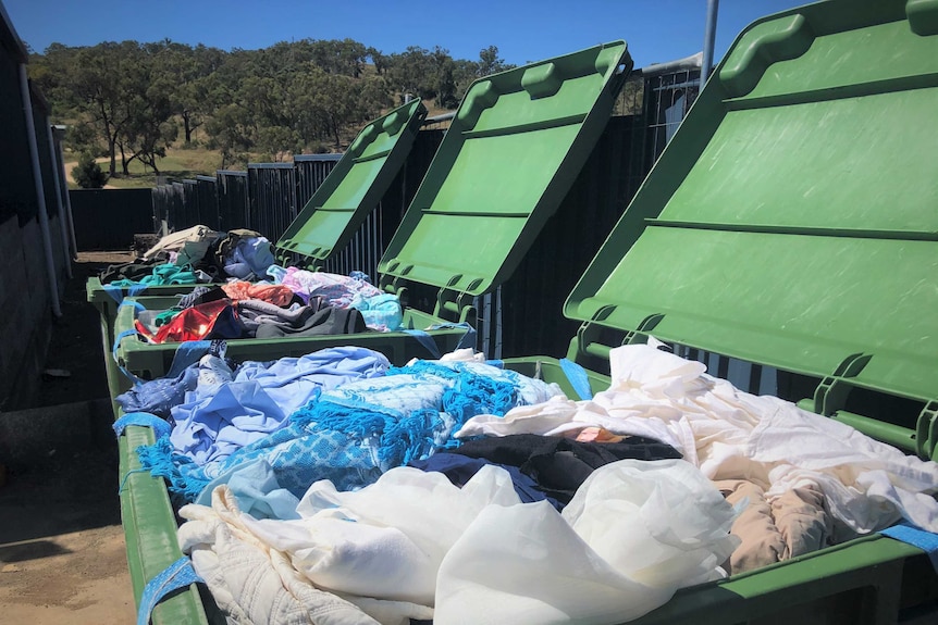 Three large green bins full of clothing.