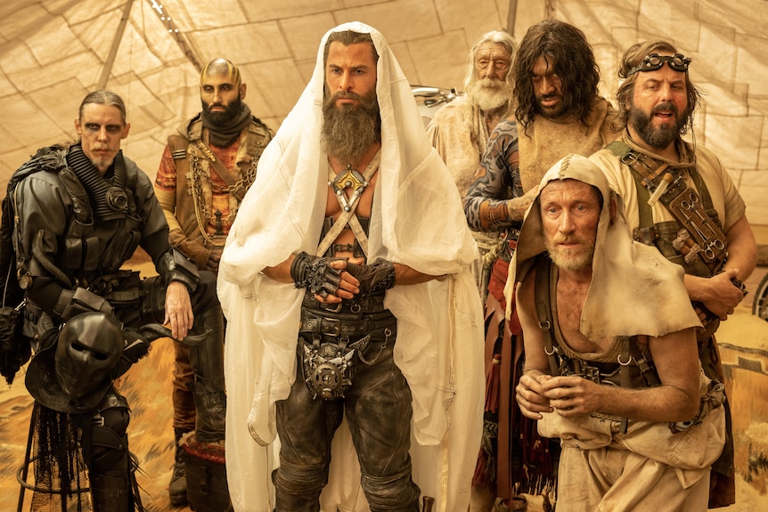 Chris Hemsworth flanked by a group of men, all in costume in film still.