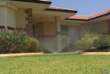 A sprinkler sprays water onto grass outside a house.