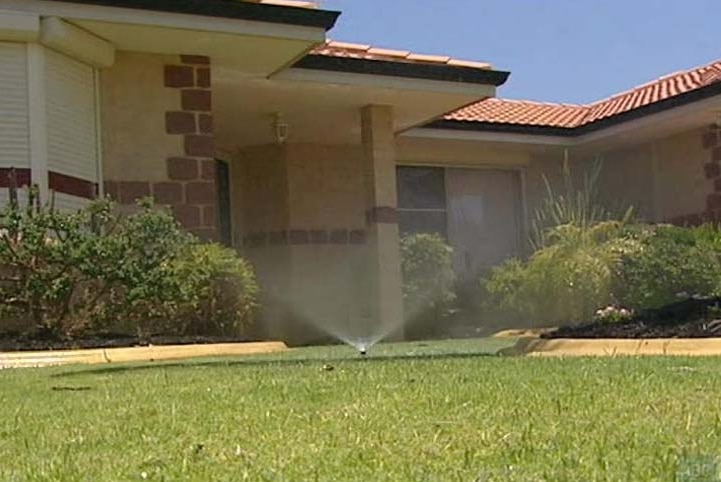 A sprinkler sprays water onto grass outside a house.