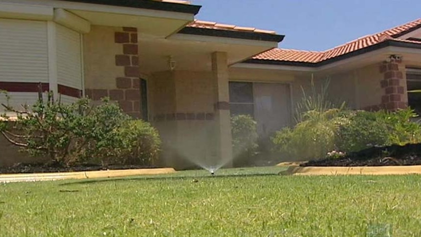 A sprinkler sprays water onto grass outside a house.