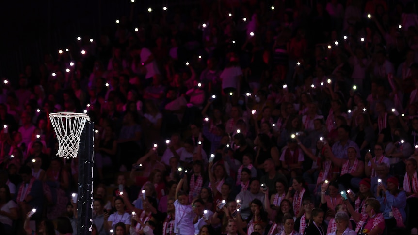 Lights shine in the crowd with a netball hoop in the foreground
