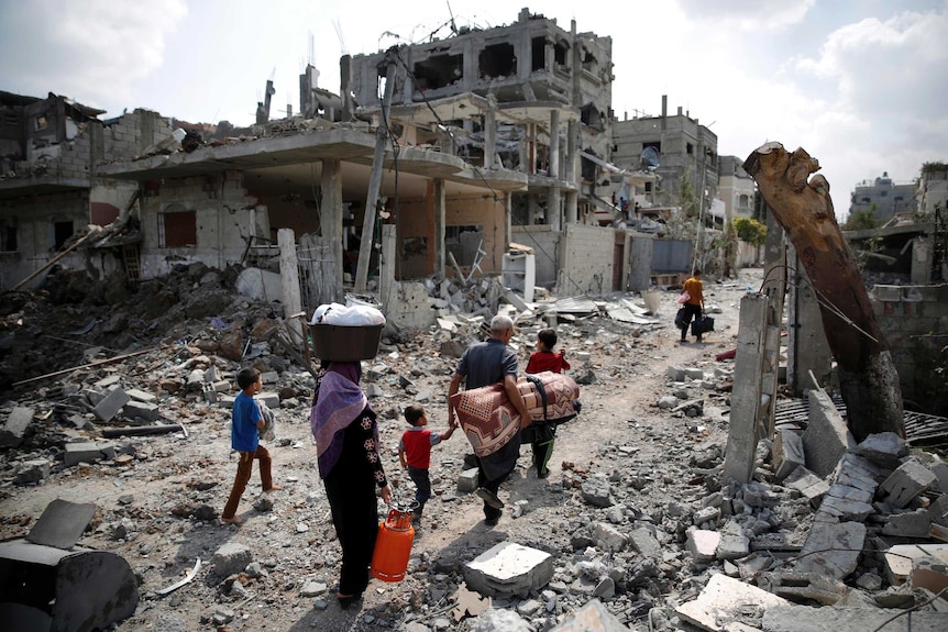 A Palestinian family carries their belongings towards the remains of their destroyed home