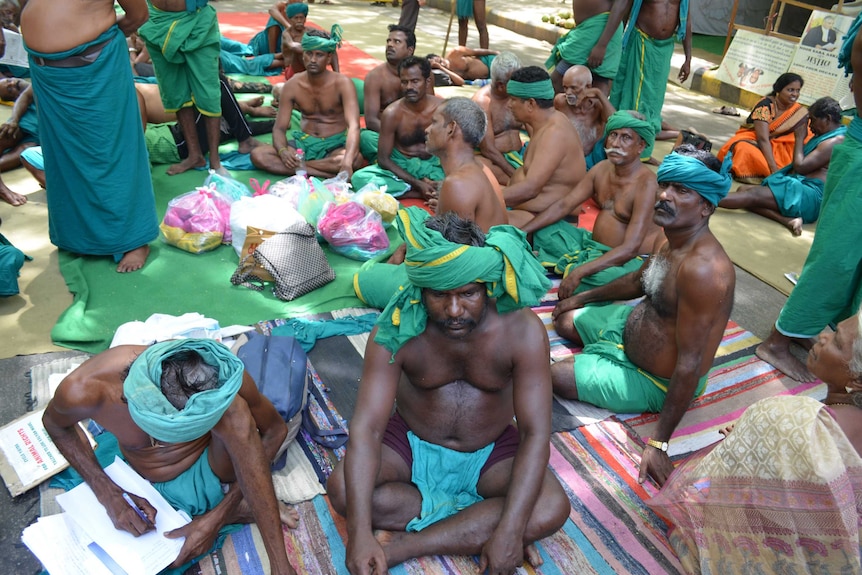 Farmers sit on rugs mostly dressed only in sarongs, protesting in Delhi.