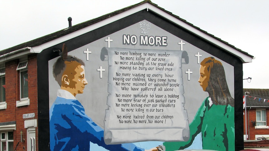 You see a large peace mural painted on the side of a brick tenement on an overcast day, headline reading, 'No More'. 