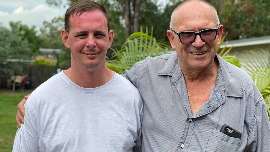 Two men, one older and with glasses, look at the camera.