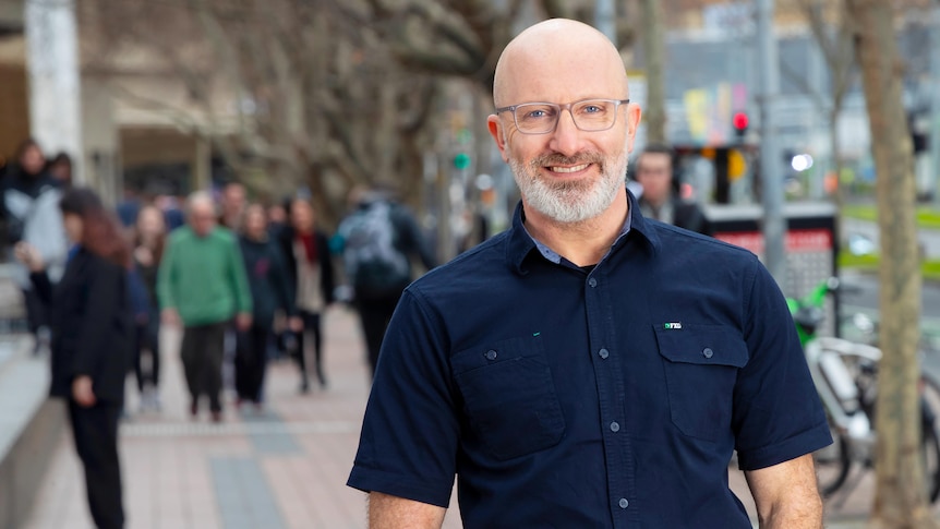 A shirt-sleeved ABC Radio Melbourne presenter Raf Epstein, hands in pockets, photographed smiling on a city street.