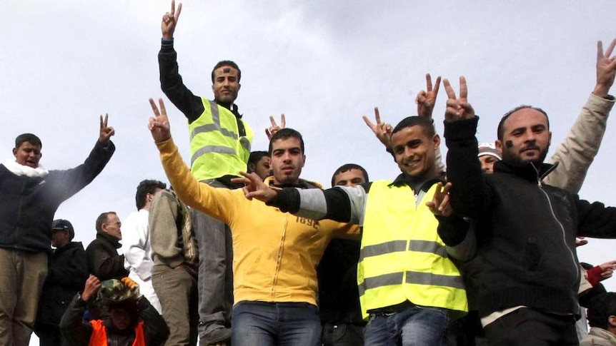 Anti-government protesters make victory signs as they stand on an army tank in Benghazi