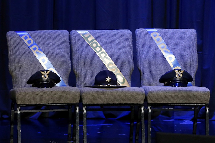 Three chairs, each with a police officer's hat on it, sit on stage during a memorial in Baton Rouge.