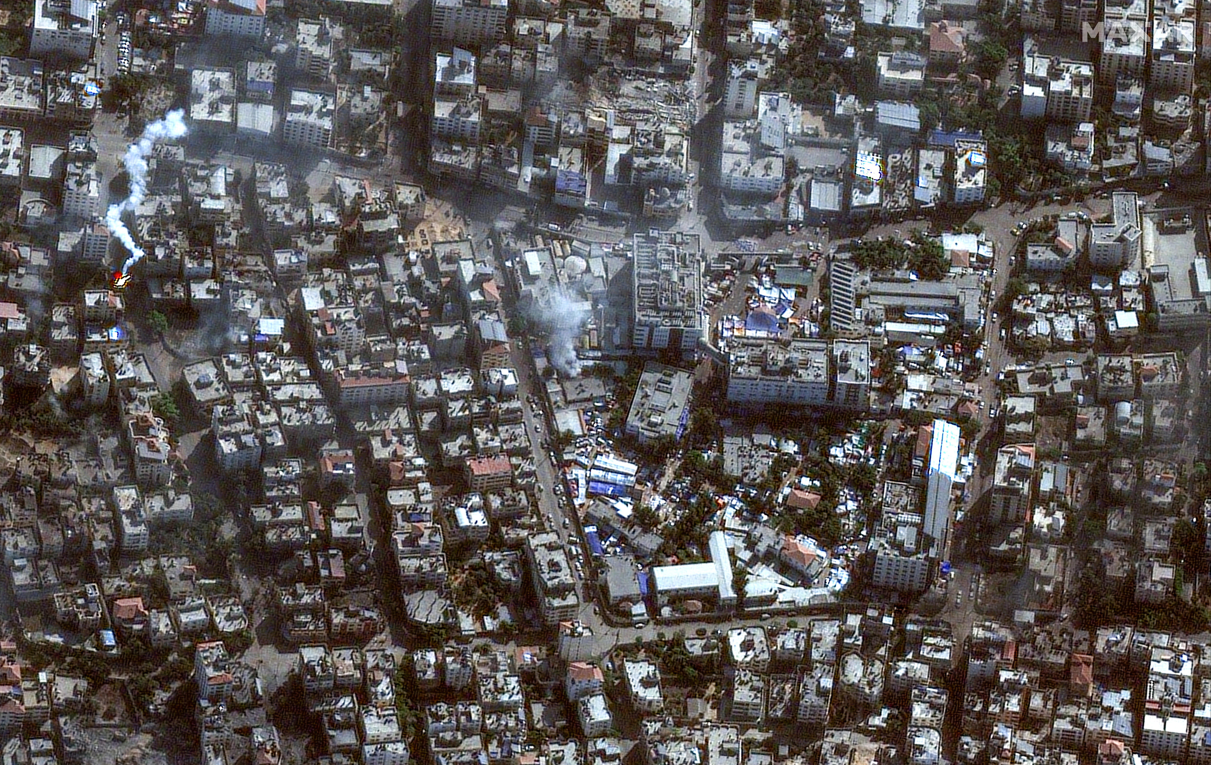 A satellite image shows two clouds of smoke over a densely built urban area with a hospital complex at the centre