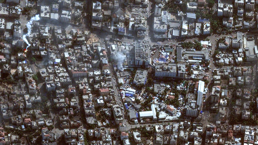 A satellite image shows two clouds of smoke over a densely built urban area with a hospital complex at the centre
