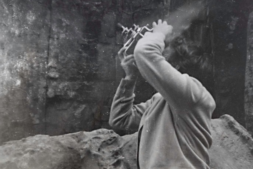 Black and white photo of woman pointing a camera upwards