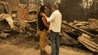A man consoling a woman in front of a burnt house.