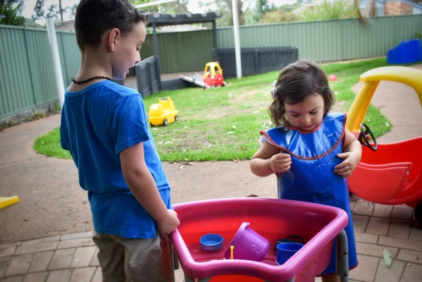 Two young children playing with colourful water toys in yard.