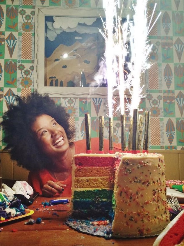 Presenter and DJ Faustina Agolley smiling, with a rainbow cake with sparklers in front of her.