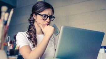 A woman wearing glasses stares at a computer.